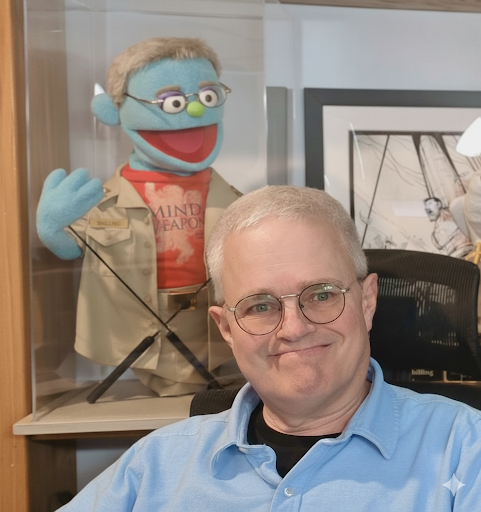 Russell Shilling at his desk with a muppet in the background.